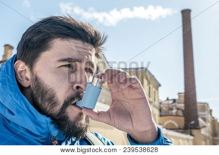 Portrait Of Young Man Using Asthma Inhaler Outdoor With Factory Chimney On Backgroung