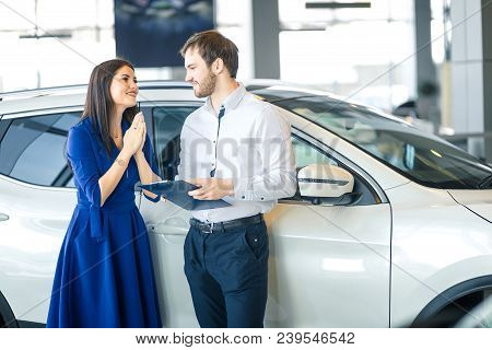 Young Happy Housewife Thanking Her Husband For His Cute Present- A New Car In Car Showroom