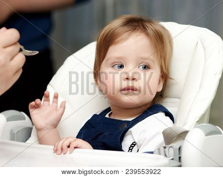 Baby Is Eating Food While Sitting At Highchair.