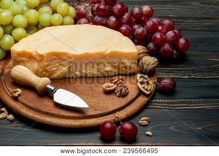 Pieces Of Parmesan Or Parmigiano Hard Cheese And Grapes On Wooden Cutting Board