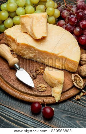 Pieces Of Parmesan Or Parmigiano Hard Cheese And Grapes On Wooden Cutting Board
