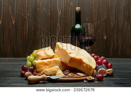 Pieces Of Parmesan Or Parmigiano Hard Cheese, Grapes And Wine On Wooden Cutting Board
