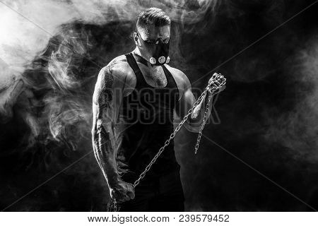 Portrait Of Muscular Sportsman In Training Mask Hold Metal Chain.black Background With Smoke