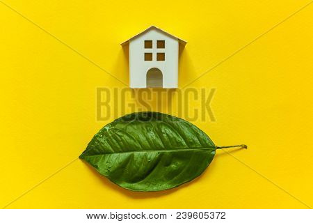 Miniature Toy Model House With Green Leaves On Yellow Colourful Trendy Backgdrop. Eco Village, Abstr