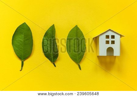 Miniature Toy Model House With Green Leaves On Yellow Colourful Trendy Backgdrop. Eco Village, Abstr