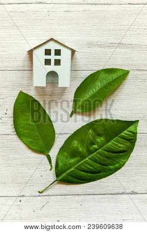 Miniature White Toy Model House With Green Leaves On Wooden Backgdrop. Eco Village, Abstract Environ