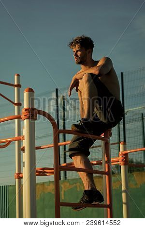 Man Sit On Metal Jungle Gym On Blue Sky. Sportsman With Bare Torso On Monkey Bars Top. Sport, Health