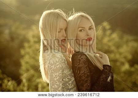 Sisters Twins Posing On Sunny Natural Landscape. Two Women With Red Lips And Long Blond Hair. Contra
