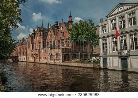 Wooded Gardens And Brick Buildings On The Canal Edge In A Sunny Day At Bruges. With Many Canals And 