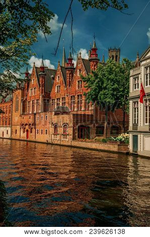 Trees And Brick Buildings On The Canal Edge In A Sunny Day At Bruges. With Many Canals And Old Build