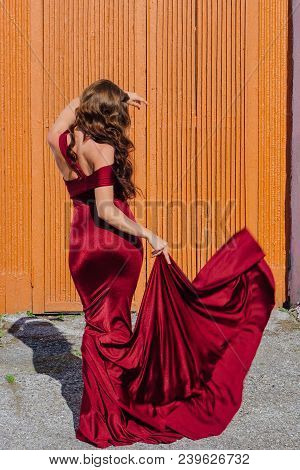 Back View Of A Beautiful Young Woman In A Long Red Evening Gown With A Train Standing Next To The Ol