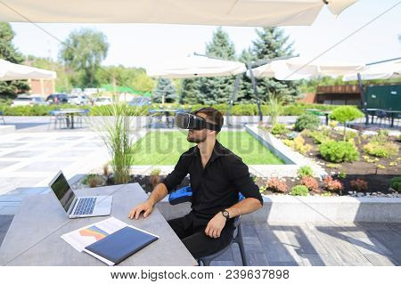 Male Freelancer Working With Papers And Laptop, Enjoying Virtual Reality Glasses In Open Air . Conce