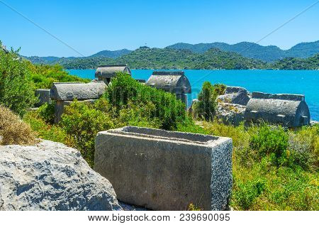 The Carved Stone Tombs Of Ancient Necropolis On The Coast Of Kekova Bay With Taurus Mountains On The
