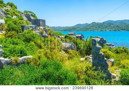 The Carved Stone Sarcophagi Of Lycian Necropolis Among The Lush Greenery, Kekova, Turkey.