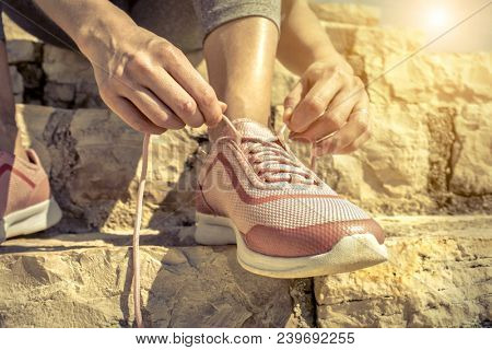 Women runner bootlace on her boot after running in sunny day under sunlight from blue sky on the stone steps.