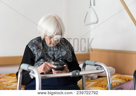 Lonley Elderly 95 Years Old Woman Sitting At The Bad Using Modern Mobile Phone Application To Monito