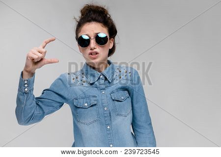 Young Girl In Round Glasses On A Gray Background. Portrait Of A Young Beautiful Girl. Charming Girl 
