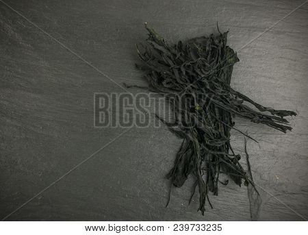 Heap Of Dry Wakame Seaweed On Black Stone Background. Healthy Algae Food With Place For Text