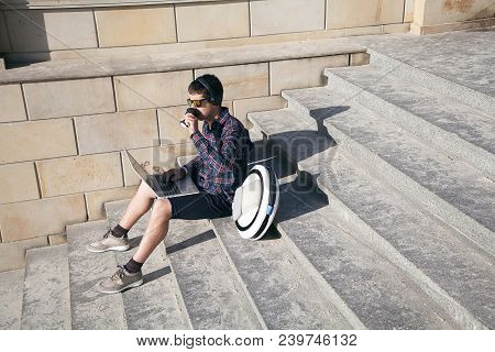 Businessman Is Sitting On The Stairs With Laptop, Mono-wheel And Drinking Coffee In His Working Brea