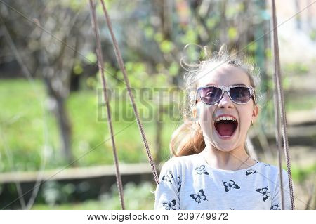 Little Child Smile On Swing In Summer Yard. Fashion Girl In Sunglasses Enjoy Swinging On Sunny Day. 