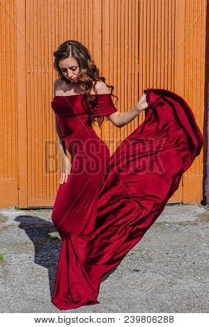Beautiful Young Woman In A Long Red Evening Gown With A Train Standing Next To The Old Door
