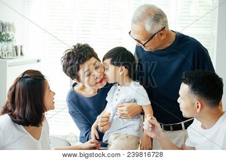 Boy Kissing Grandmother On Cheeks With The Whole Asian Family Of Three Generations Together At Home