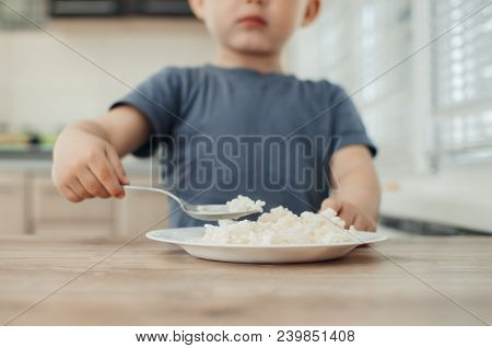 The Little Boy In The Kitchen Eagerly Eating Rice With A Spoon Independently