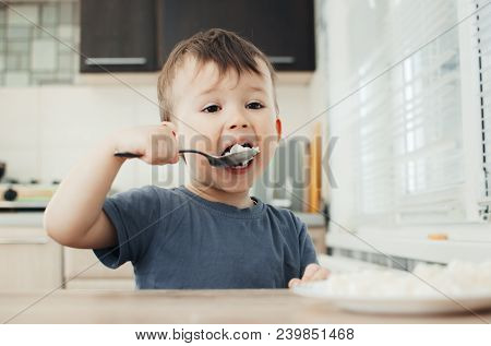 The Little Boy In The Kitchen Eagerly Eating Rice With A Spoon Independently