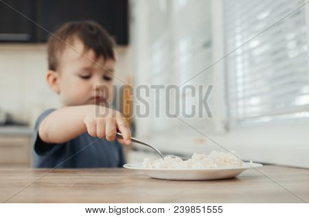 The Little Boy In The Kitchen Eagerly Eating Rice With A Spoon Independently