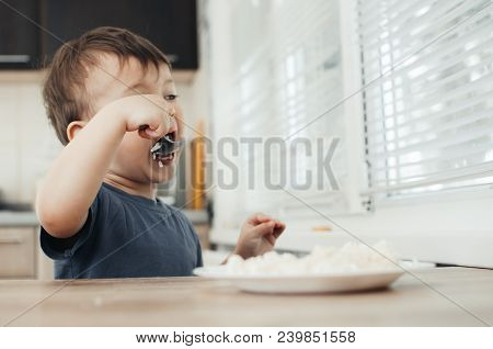 The Little Boy In The Kitchen Eagerly Eating Rice With A Spoon Independently