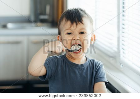 The Little Boy In The Kitchen Eagerly Eating Rice With A Spoon Independently