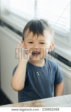 The Little Boy In The Kitchen Eagerly Eating Rice With A Spoon Independently
