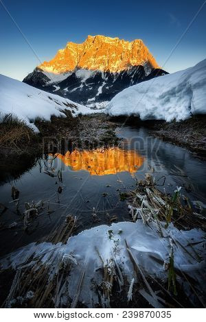 Amazing Scene Of Zugspitze Mountain. Frozen Reflection Of Peak In Cold River. Typical Winter Scene N