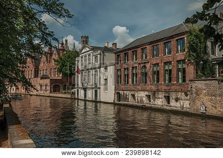 Wooded Gardens And Brick Buildings On The Canal Edge In A Sunny Day At Bruges. With Many Canals And 