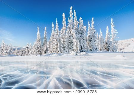Blue Ice And Cracks On The Surface Of The Ice. Frozen Lake Under A Blue Sky In The Winter. The Hills