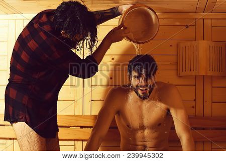 Handsome Man In Red Checkered Shirt Pours Water From Bucket On Head Of Cheerful Young Male Bather Wi