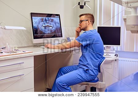 Male Dentist Looking At Teeth X-ray On The Computer In A Dentist Office.