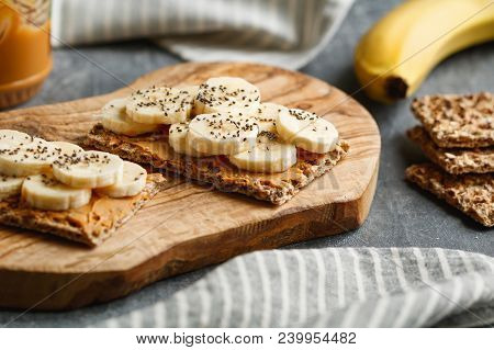 Two Multi Grain Breads With Peanut Paste, Banana Slices And Chia Seeds On A Serving Wooden Board. Th