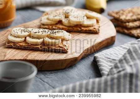 Two Multi Grain Breads With Peanut Paste, Banana Slices And Chia Seeds On A Serving Wooden Board. Th