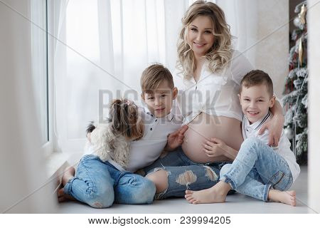 Two Boys, Brothers, Stand Next To A Beautiful Pregnant Mother,holding Hands On The Belly Of A Pregna