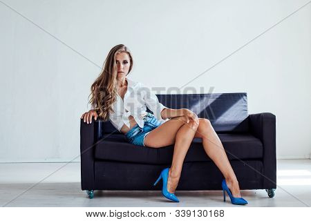 Beautiful Blonde Girl With Blue Eyes Sitting On The Couch In A White Room 1