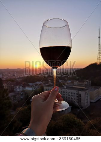 Wine Swirl With A Sky And Sunset. Wineglass With Woman Hand Swirling Rose Red Drink Outdoor During H