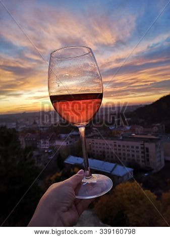 Wine Swirl With A Sky And Sunset. Wineglass With Woman Hand Swirling Rose Red Drink Outdoor During H