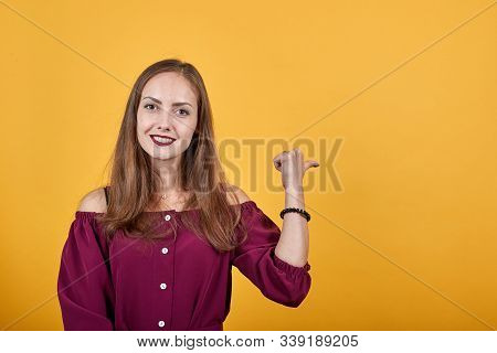 Girl In Burgundy Bluse Over Isolated Orange Background Pointing Finger To Right With Smile