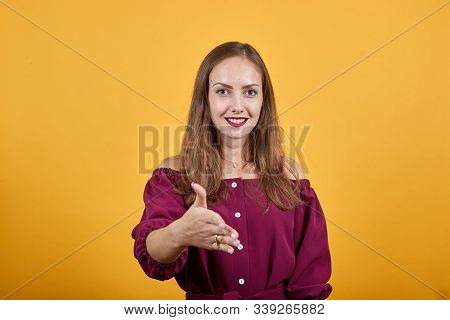 Ginger Girl In Burgundy Bluse With Bow Over Isolated Orange Background With Smile On Face Giving Han