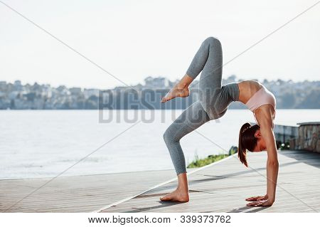 Her Hobby. Young Woman With Slim Type Of Body Does Exercises Against Lake.