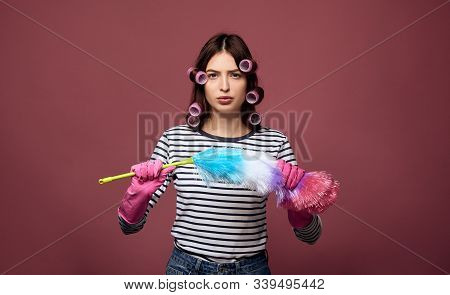 A Serious Lady In Curlers Holds A Dust Brush In Her Hands.