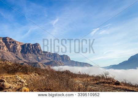 The Tops Of The Mountains Against A Bright Blue Sky. And Down In The Valley Lies A Thick Fog.