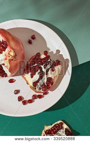 Sliced Pomegranate On A White Plate On A Green Background Close-up