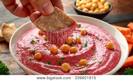 Man Hand Is Picking Some Beetroot Hummus Dip With Chickpea, Olive Oil, Lemon, Carrots And Pita Bread
